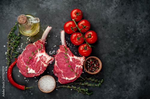 two raw steaks, beef tomahawk with spices, tomatoes and thyme on a stone background. with copy space for your text