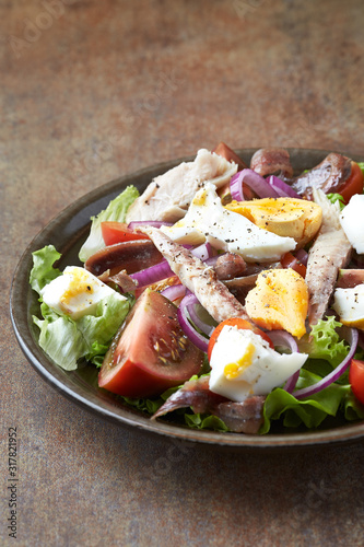  Salad with hard-boiled eggs, tomatoes, lettuce, red onion and mackerel on rustic background.