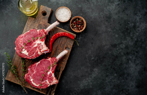 two raw steaks, beef tomahawk with spices, thyme on a stone background. with copy space for your text