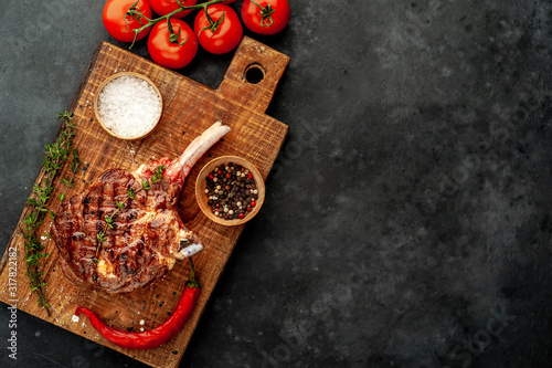 grilled beef steak - tomahawk with spices, tomatoes, thyme on a stone background. with copy space for your text