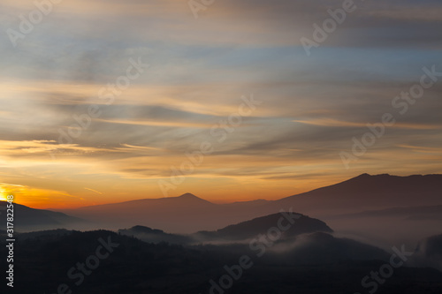 Valley filled with soft mist, distant silhouettes of impressive mountains and amazing colors of vivid morning sky © Nikola