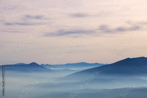 Pastel color palette of misty landscape with rocky mountain peak rising above fog covered valleys and mountain layers during colorful 