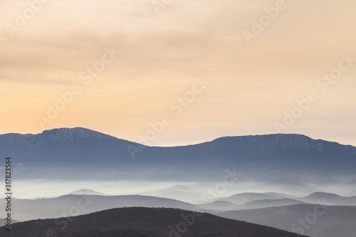 Pastel color palette of misty landscape with rocky mountain peak rising above fog covered valleys and mountain layers during colorful  © Nikola