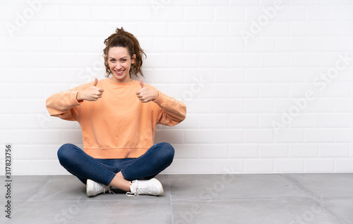 Young woman with curly hair sitting on the floor giving a thumbs up gesture