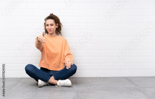 Young woman with curly hair sitting on the floor handshaking after good deal