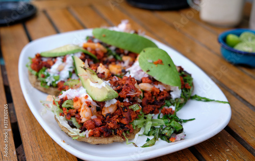 Mexican tostada with topping of minced sausage and shrimp, with avocado on top, on a white plate