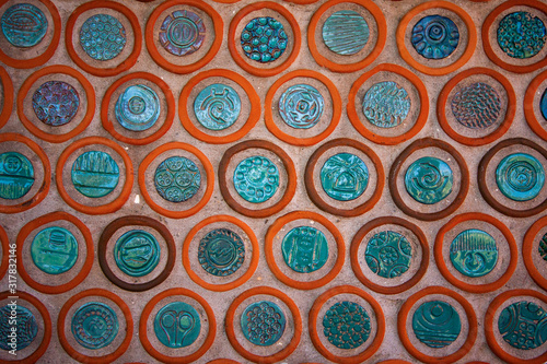 Wall decorated with a pattern of round ceramic plates. Brick-orange circles and glazed dark blue plaques inside them. Medium pattern.