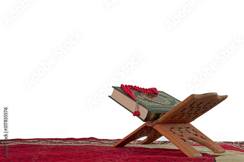 Selective focus of Holy Quran with arabic calligraphy meaning of Al Quran and red tasbih or rosary beads over white background.
