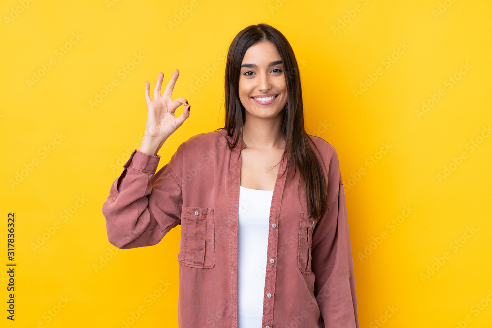 Young brunette woman over isolated yellow background showing ok sign with fingers Young brunette woman over isolated yellow background showing ok sign with fingers