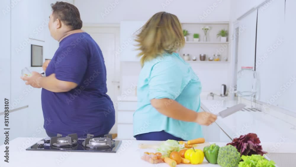 Happy overweight woman and her husband making salad while dancing in the studio. Shot in 4k resolution