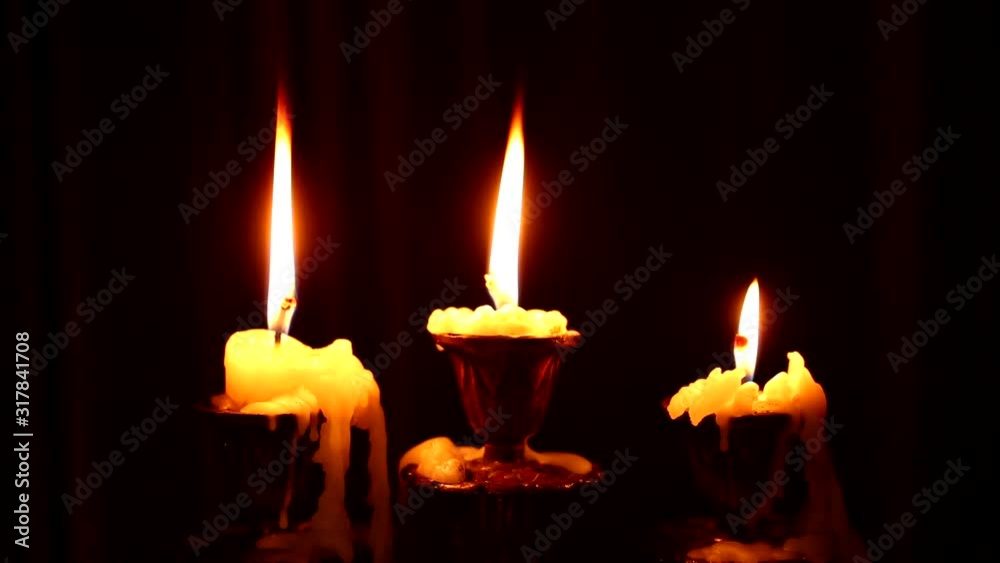 Three candles burn in a candlestick on black background. Wax dripped from a burning candle. Antique gothic candlestick. Candles are burning for the holiday. Gothic background