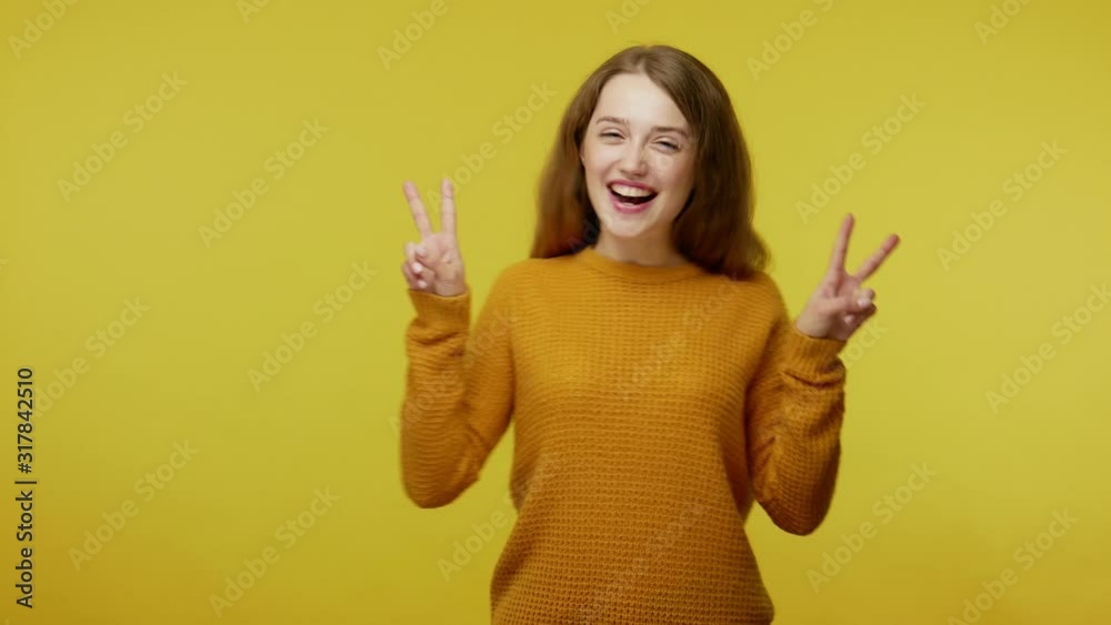 Happy joyful pretty girl in casual outfit showing victory gesture with fingers, making double v sign and mp4ing in winner dance, enjoying success. indoor studio shot isolated on yellow background Happy joyful pretty girl in casual outfit showing victory gesture with fingers, making double v sign and mp4ing in winner dance, enjoying success. indoor studio shot isolated on yellow background