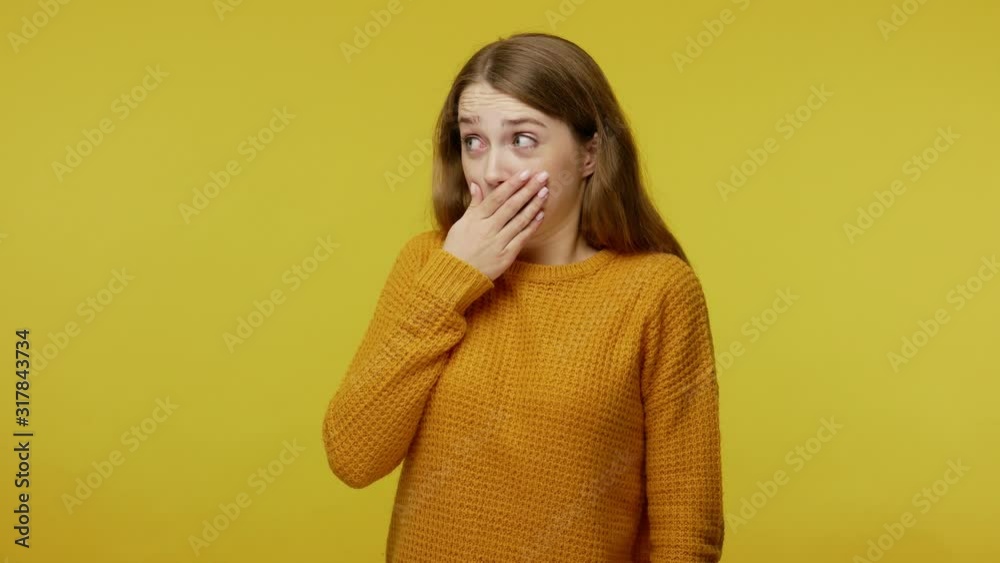 Amazed girl in casual clothes looking around and covering her mouth with hand, wondered about secret, waving head saying no, won't tell anyone. indoor studio shot isolated on yellow background Amazed girl in casual clothes looking around and covering her mouth with hand, wondered about secret, waving head saying no, won't tell anyone. indoor studio shot isolated on yellow background
