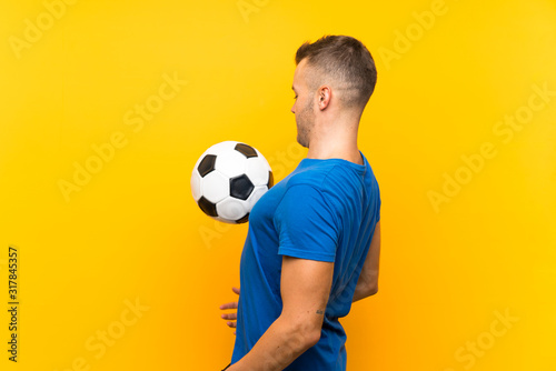Young handsome blonde man holding a soccer ball over isolated yellow background © luismolinero