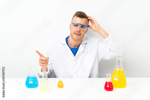 Young scientific with lots of laboratory flask surprised and pointing finger to the side