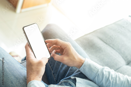 Mockup image blank white screen cell phone.men hand holding texting using mobile on sofa at home. background empty space for advertise text.people contact marketing business and technology