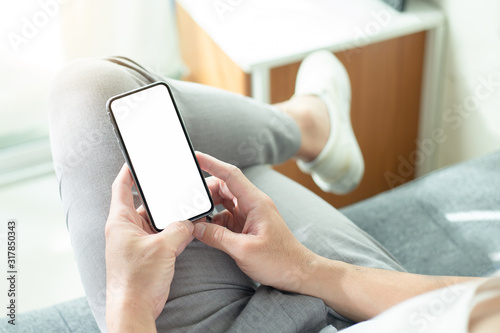 Mockup image blank white screen cell phone.men hand holding texting using mobile on sofa at home office. background empty space for advertise text.people contact marketing business and technology