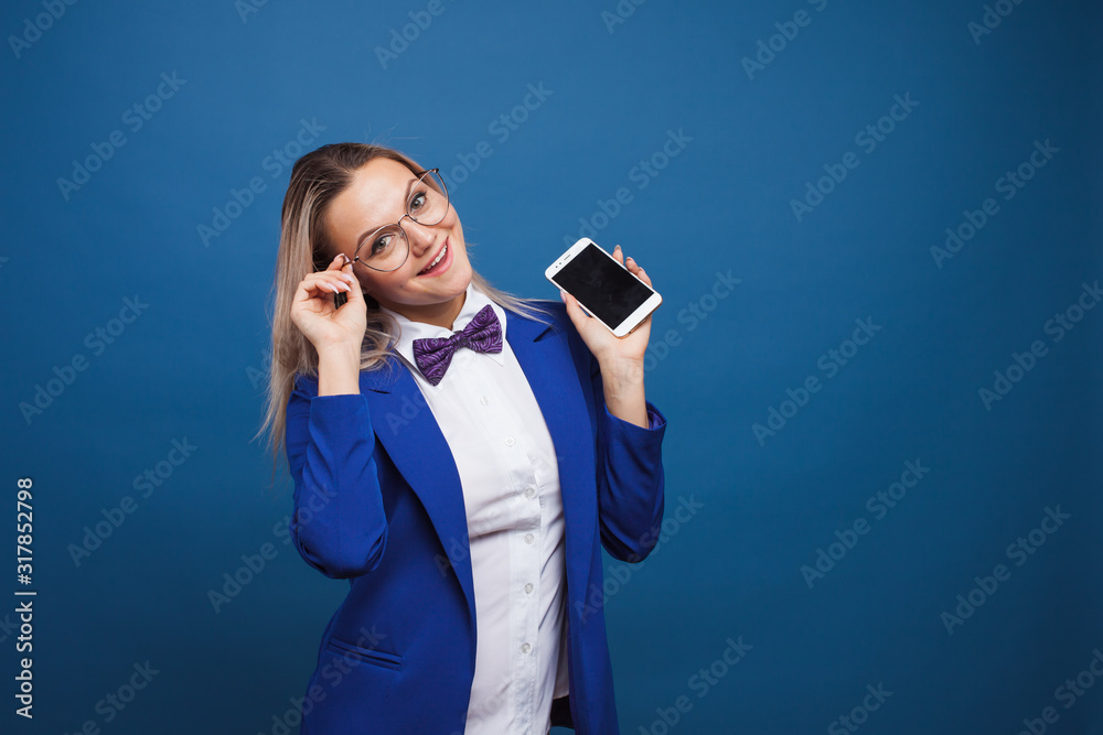 Cute and funny businesswoman in a stylish blue jacket and bow tie uses a smartphone.