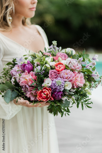 Woman holding in hands big wedding bouquet close up. Red and pink tulips, roses, purple peony. Pastel colored, floristic concept.