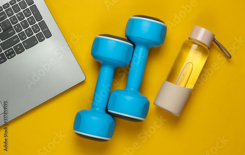 Fitness concept. Online training for a coaching profession. Laptop, dumbbell, bottle of water on yellow background. Top view