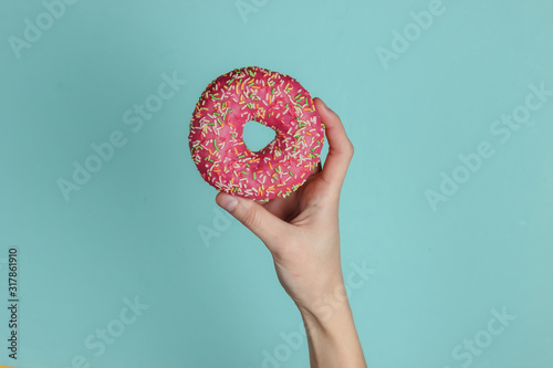 Female hand holds a glazed donut on a blue background. Pastel color trend. Top view.