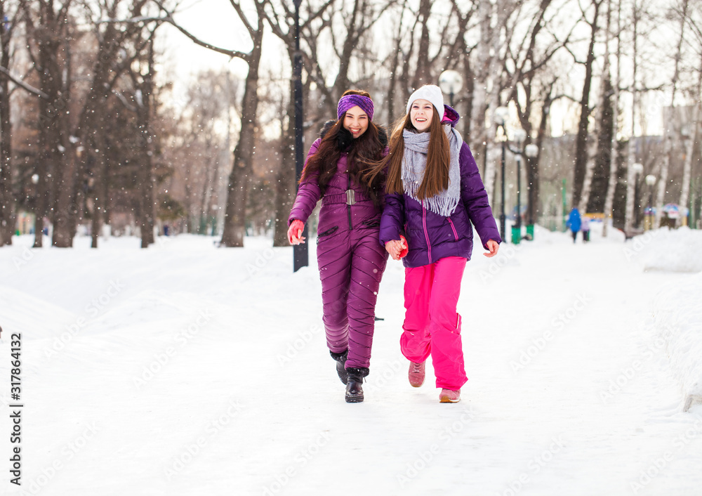 Fototapeta premium Two happy beautiful girlfriends walk in the winter in a city park