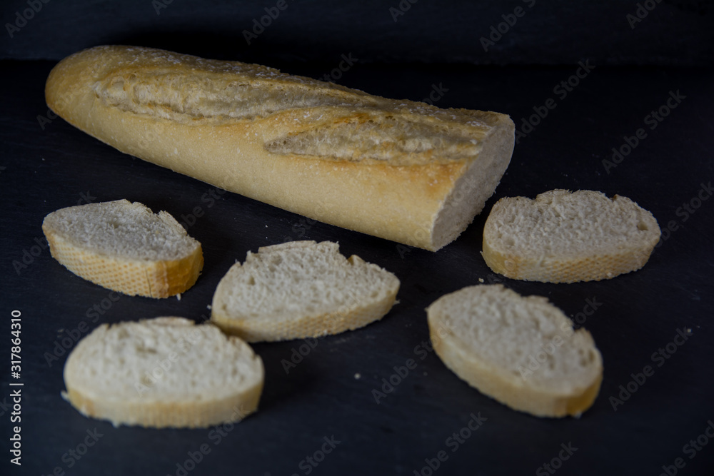 Barra de pan con rebanadas cortadas sobre una bandeja negra de piedra