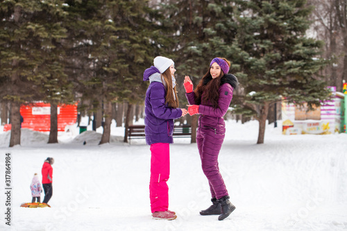 Portrait of two young beautiful women in ski suit posing in winter in the park
