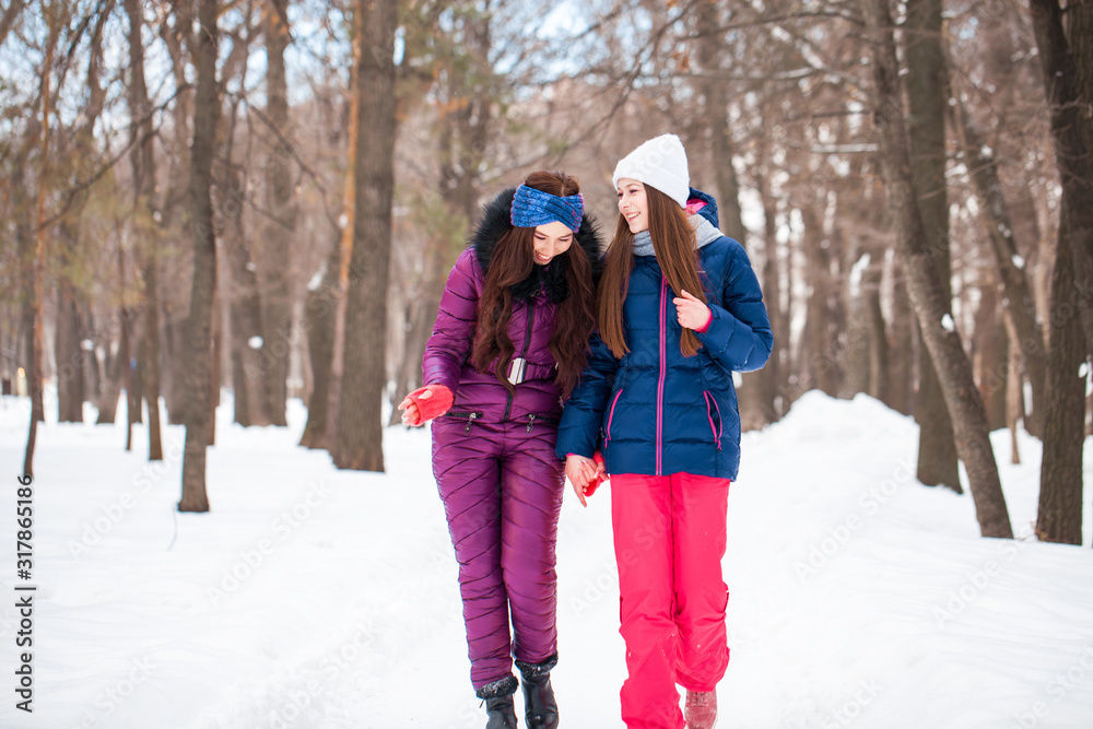Portrait of two young beautiful women in ski suit posing in winter in the park