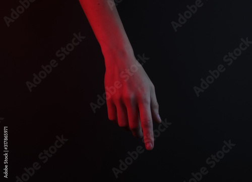 Female hand touches something on a black background. Red neon night light