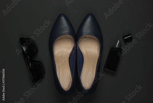 Women's accessories on a black background. High heel shoes, perfume bottle, sunglasses. Top view