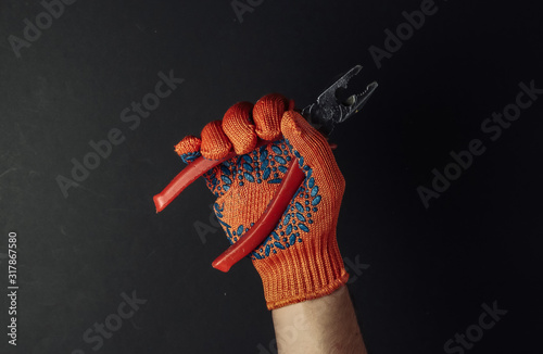 Hands with work gloves are holding pliers on black background. Industrial worker