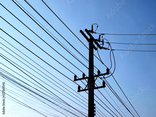 Silhouettes of high tension and low tension power lines on poles. On the bright blue morning sky background with copy space. Selective focus