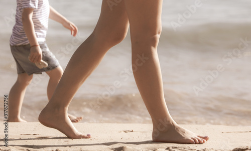 Legs of a woman and a boy on the sand by the sea