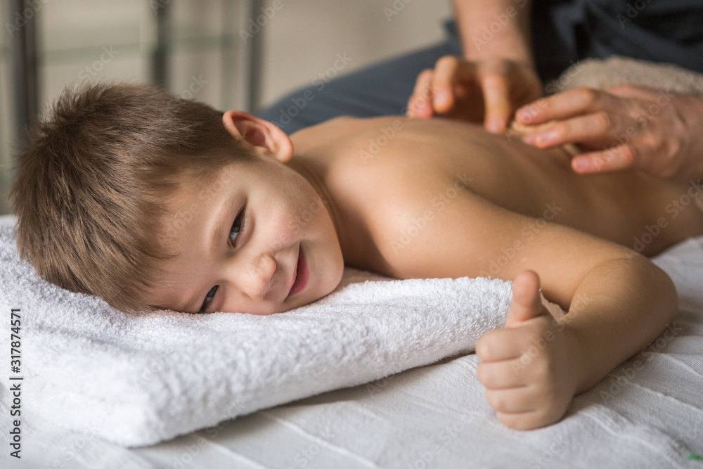 Boy toddler relaxes from a therapeutic massage. Physiotherapist working with patient in clinic to the back of a child Boy toddler relaxes from a therapeutic massage. Physiotherapist working with patient in clinic to the back of a child