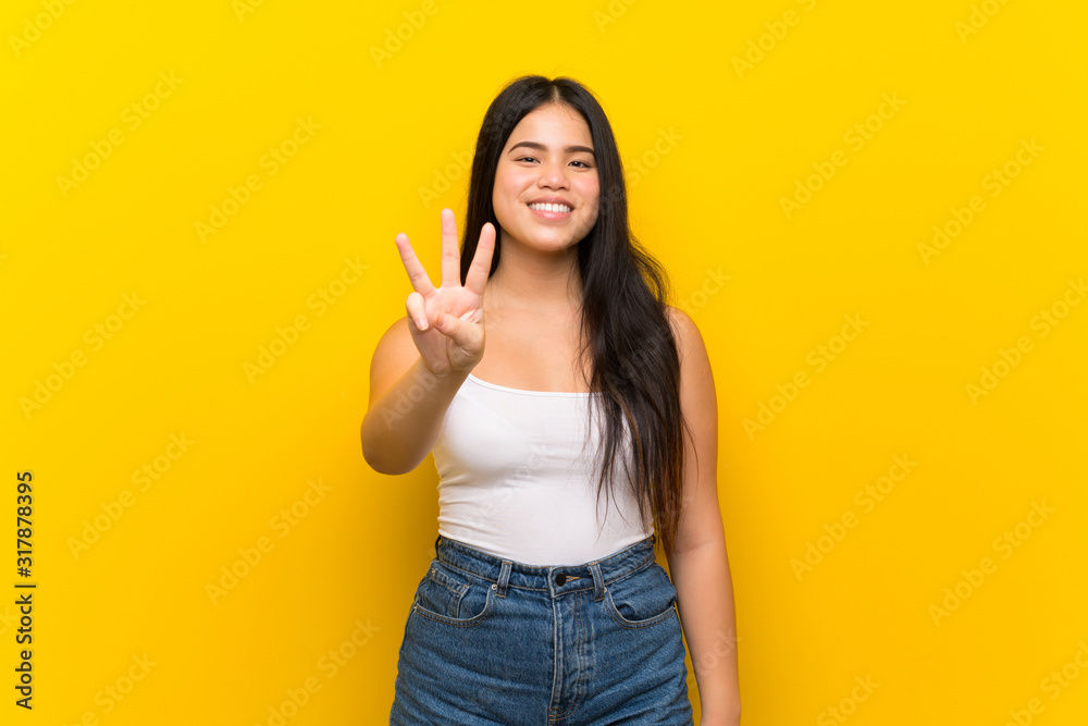 Young teenager Asian girl over isolated yellow background happy and counting three with fingers Young teenager Asian girl over isolated yellow background happy and counting three with fingers