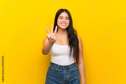 Young teenager Asian girl over isolated yellow background happy and counting three with fingers