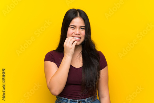Young teenager Asian girl over isolated yellow background nervous and scared © luismolinero