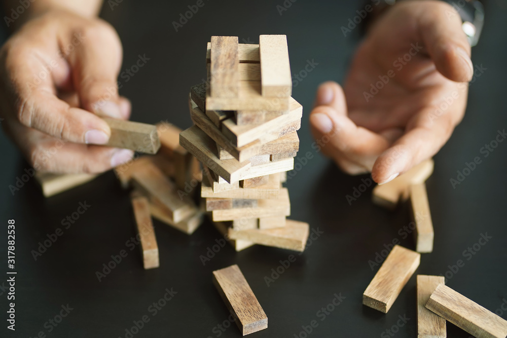 Engineer hand cover wooden block and piling up and stacking a wooden block tower on black desk. planning, risk and strategy in business concept. Engineer hand cover wooden block and piling up and stacking a wooden block tower on black desk. planning, risk and strategy in business concept.