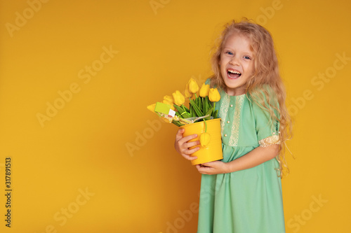 Cute cheerful girl in a green dress on a yellow background holds tulips in her hands and laughs merrily.