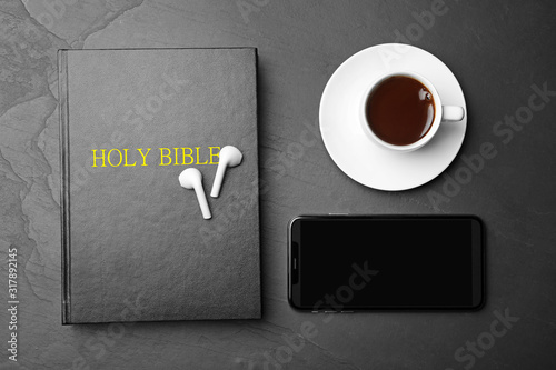 Bible, phone, cup of coffee and earphones on black background, flat lay. Religious audiobook