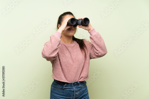 Young teenager Asian girl over isolated green background with black binoculars