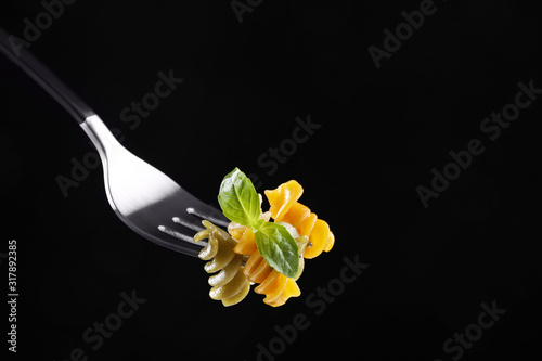 Fork with delicious spiraline pasta on black background