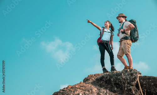 Young asian couple hikers climbing up on the peak of mountain. Two people hikers on top of the mountain enjoying valley view. Tourists with backpacks. Climbing ,Helps and team work concept