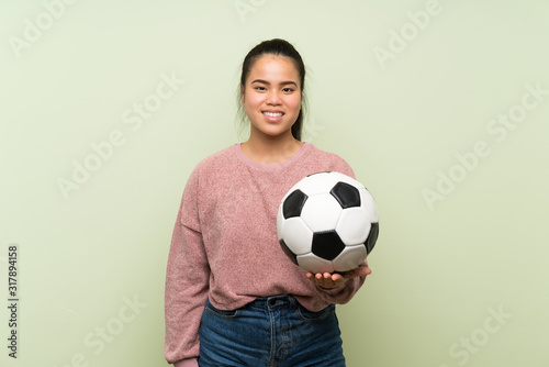 Young teenager Asian girl over isolated green background holding a soccer ball