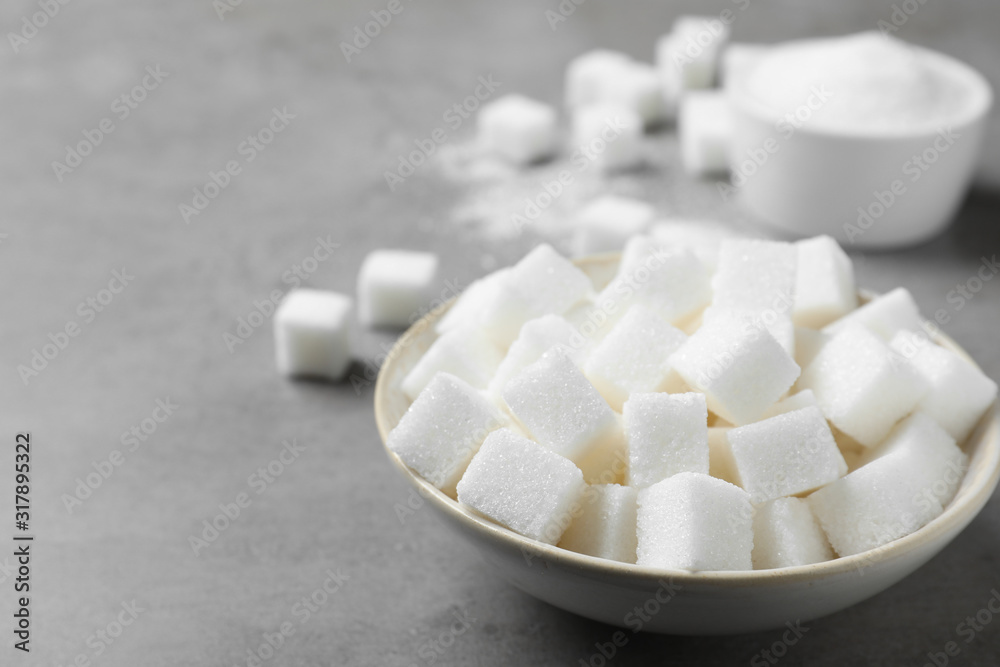 Refined sugar cubes in bowl on grey table Refined sugar cubes in bowl on grey table