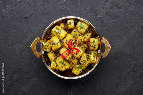 Aloo Methi in copper kadai, bowl at dark slate background. Aloo Methi is indian cuisine dish with Potato, Fenugreek and Spices. Indian Food. Copy space. Top view
