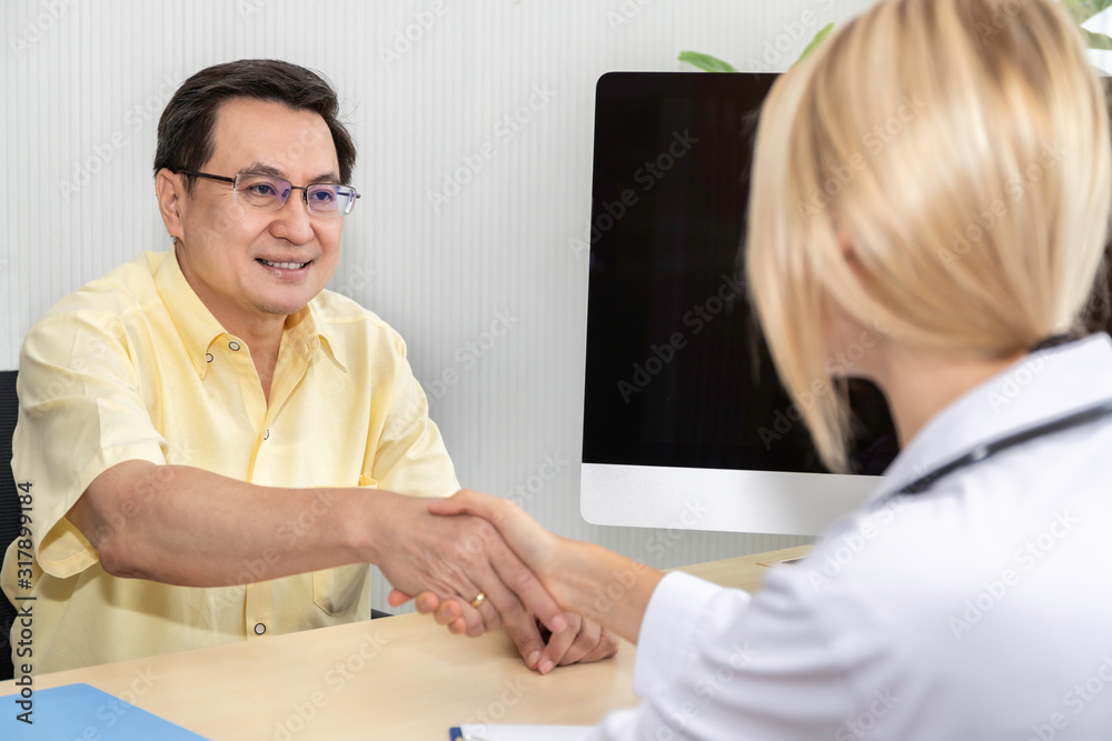 Obraz premium Smiling Caucasian woman confident doctor shaking hands with senior Asian patient in the hospital room.