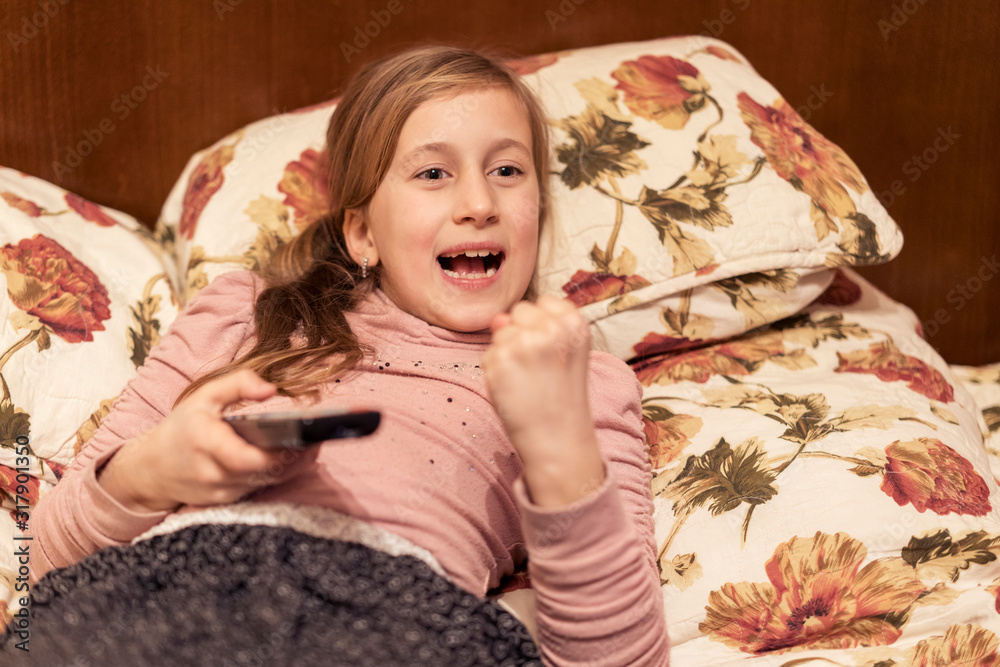 Little girl is watching tv in her bed. Little girl watching tv. Teen girl eating popcorn in front of the TV. toned Little girl is watching tv in her bed. Little girl watching tv. Teen girl eating popcorn in front of the TV. toned
