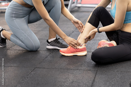 Asian young woman having ankle pain after workout at the gym. painful during exercise training and friends are here to help, encouragement